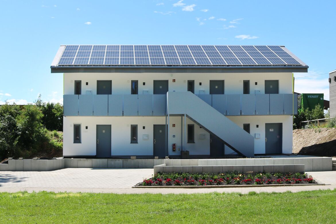 Zweistöckige modulare Unterkunft mit Außentreppe und Solarpanelen auf dem Dach.